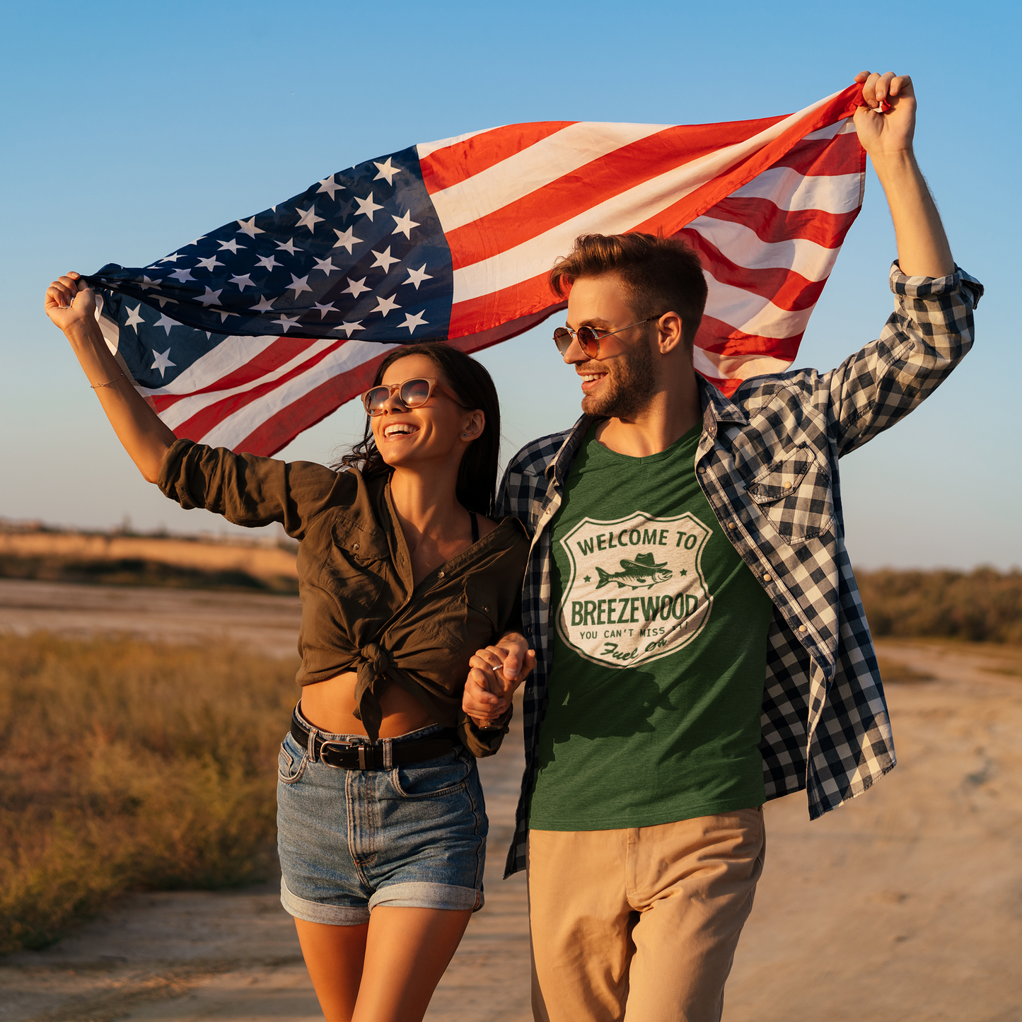 All American Couple holding a flag - Man is wearing a dark green Welcome to Breezewood Highway Sign T-Shirt - Shirt reads Welcome to Breezewood - You Can't Miss It! - Fuel On.