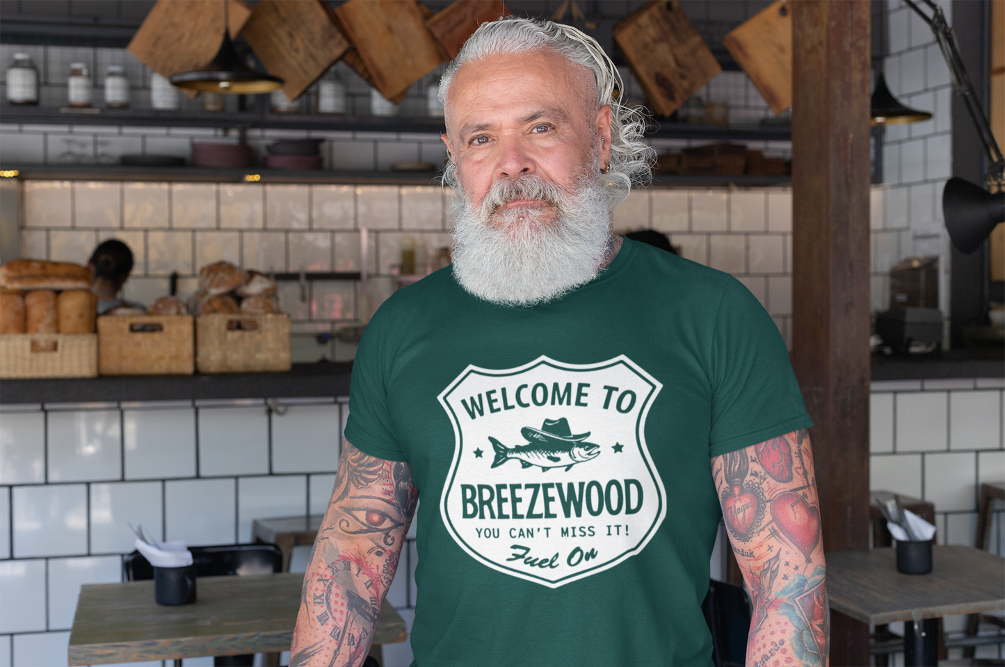 Old man standing in a bar wearing a dark green Welcome to Breezewood Highway Sign T-Shirt - Shirt reads Welcome to Breezewood - You Can't Miss It! - Fuel On.