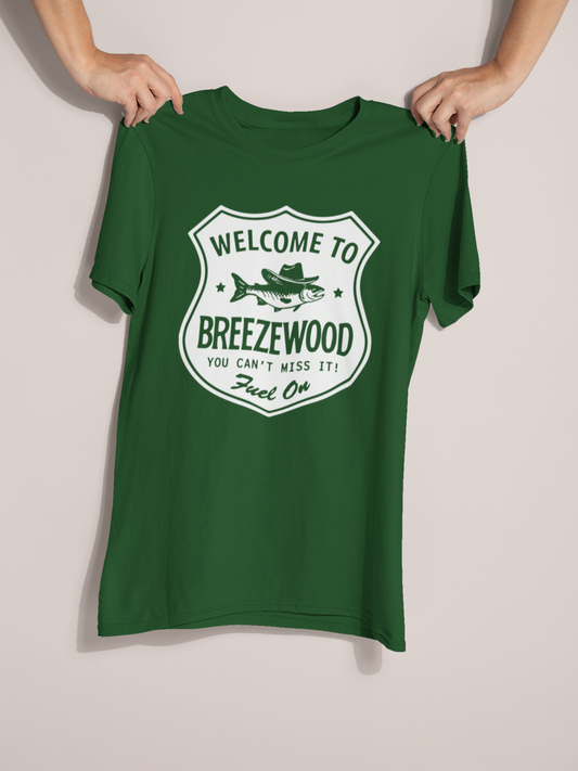 Welcome to Breezewood Highway Sign T-Shirt - Hands holding up a dark green tee displaying screen printed shirt that reads Welcome to Breezewood - You Can't Miss It! - Fuel On.